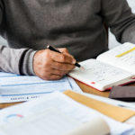 Man writing in notebook on a desk full of business papers