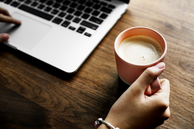 Woman on computer holding a coffee cup