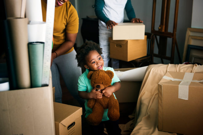 Smiling African Heritage Child Hugging Teddy Bear in New Home Living Room