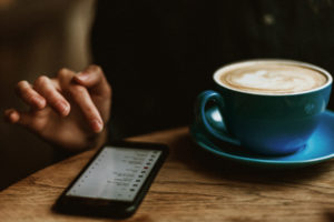 Woman using her smart phone at a coffee shop with latte