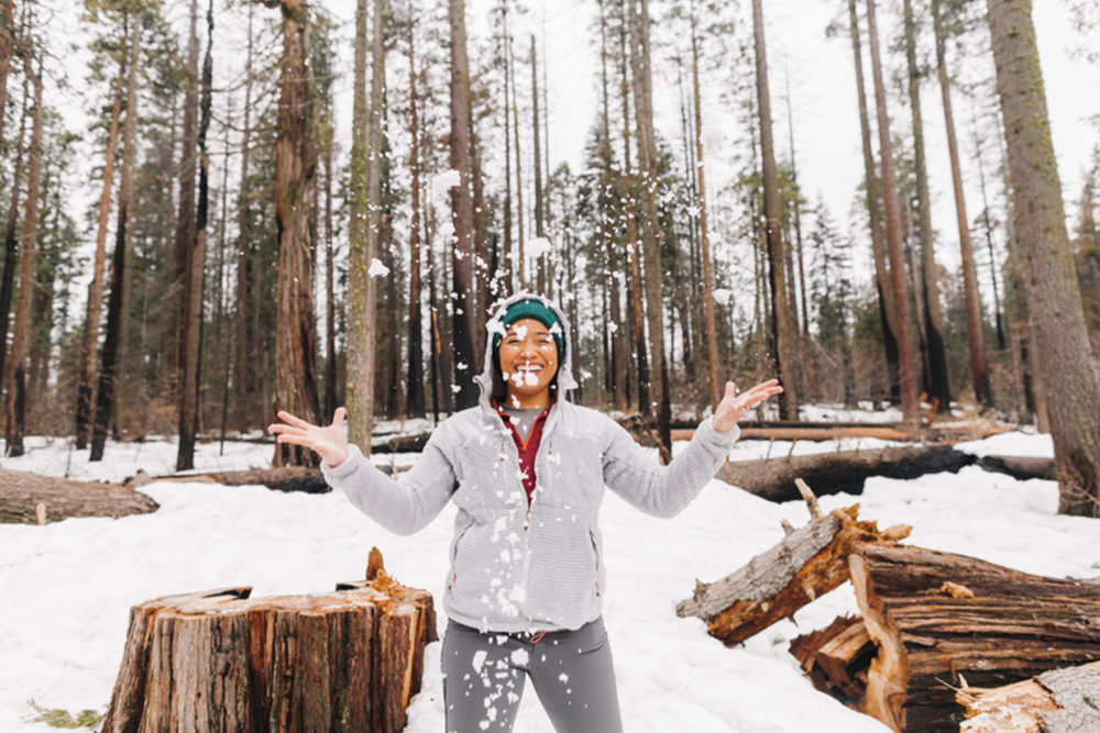 Woman throwing snow in the air at a campground in the forest