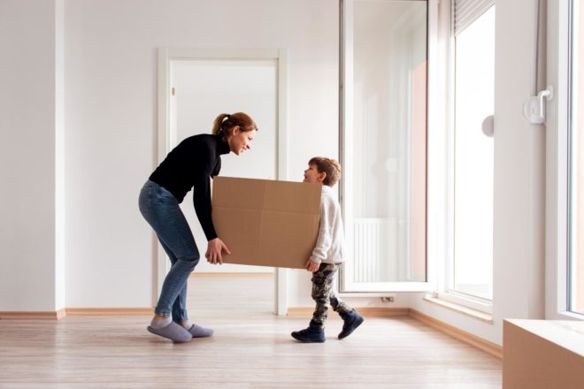 A parent and child lifting a box as they move into a new house