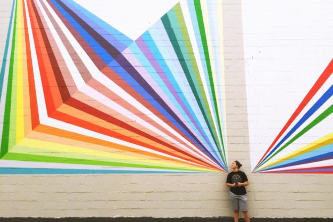 Woman wearing pride shirt by rainbow mural in PNW