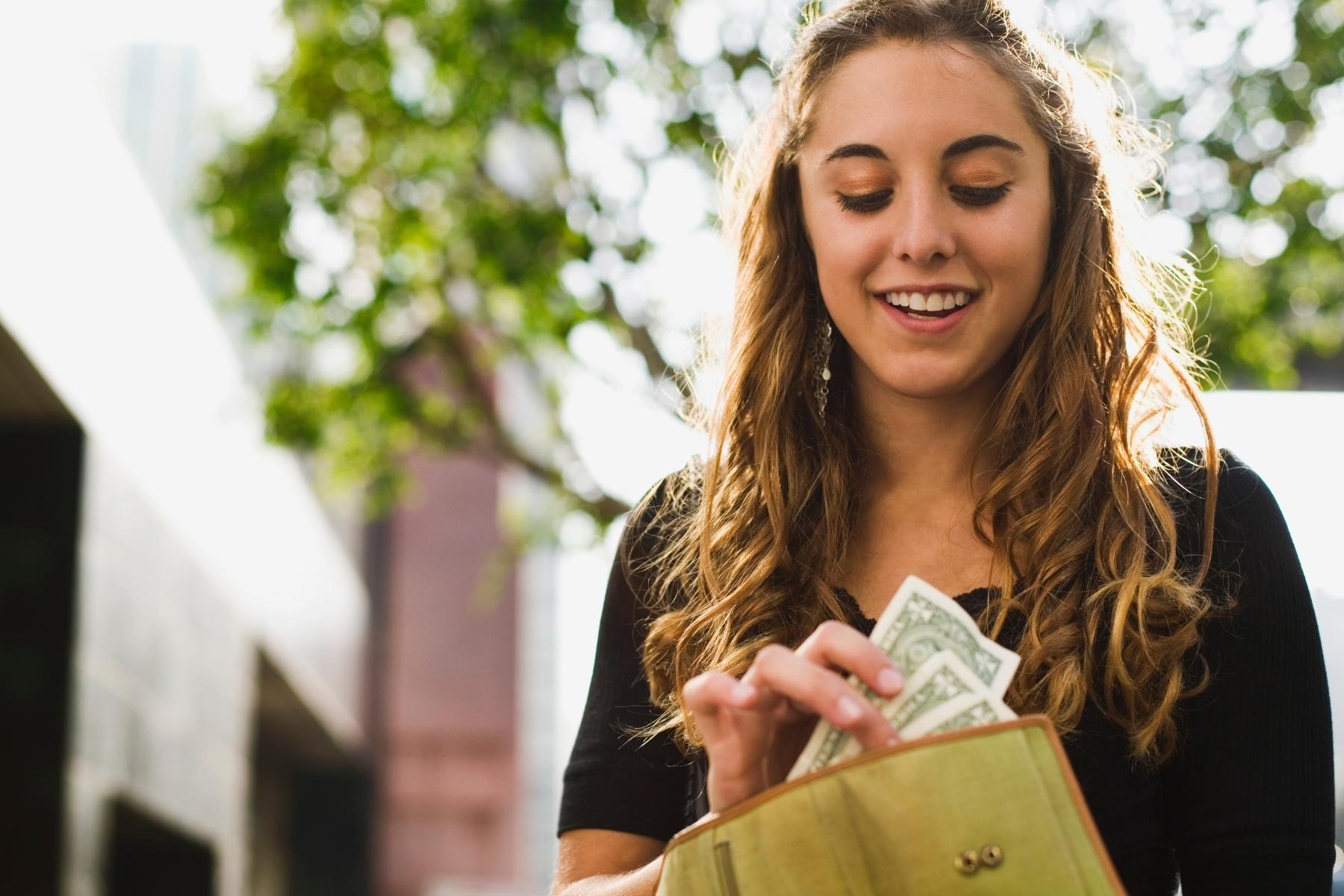 Young woman placing cash into her wallet