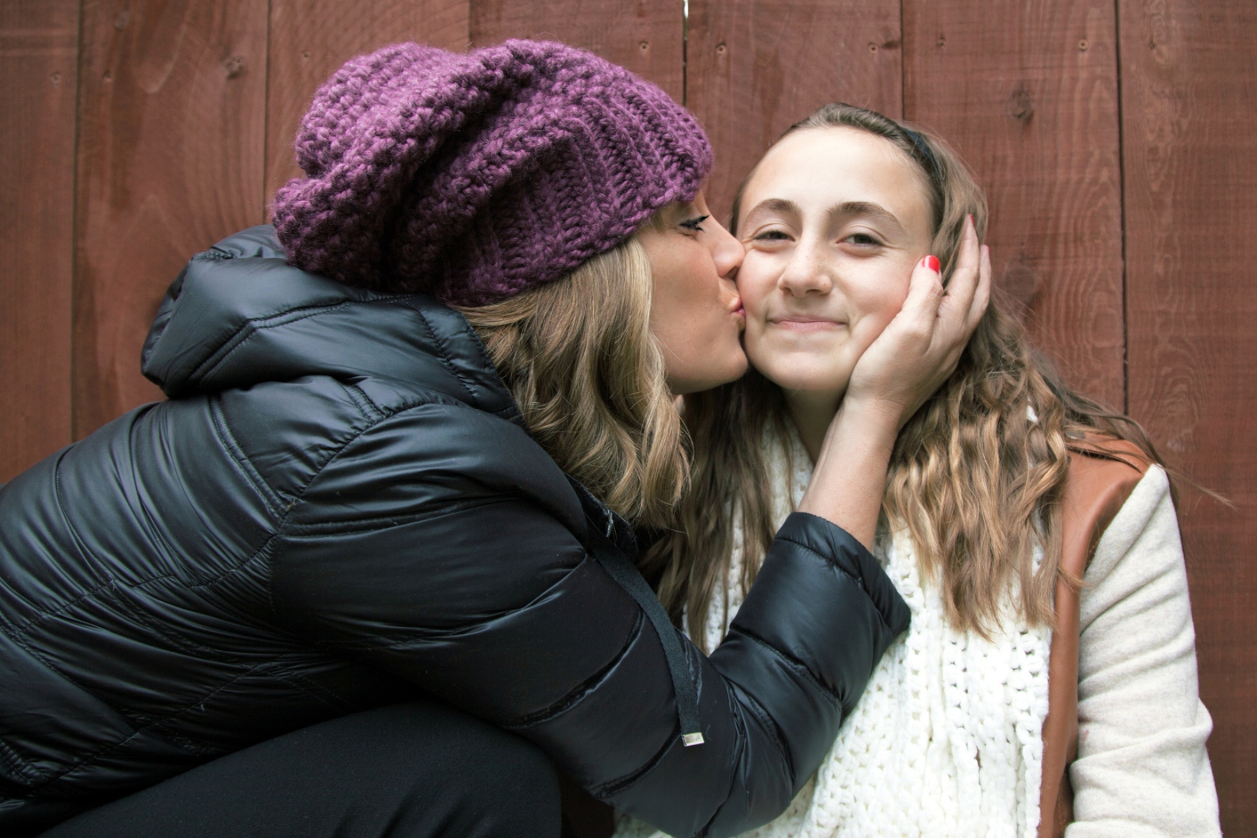 A mother kissing the cheek of her teenage daughter