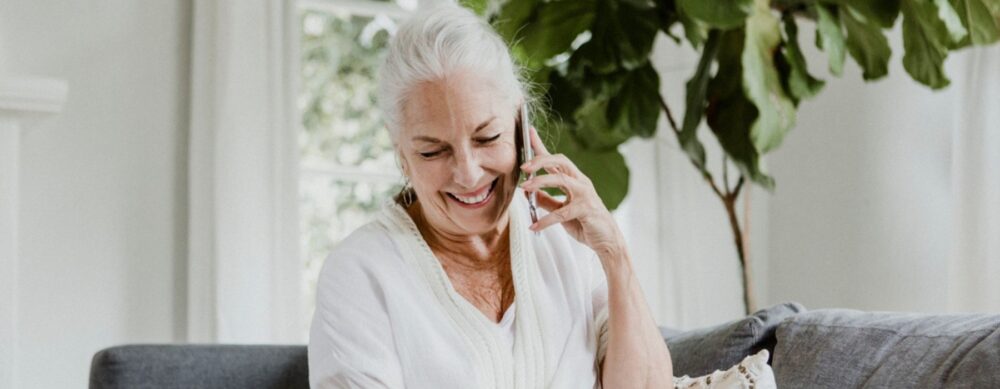 Woman sitting on couch writing notes while on the phone.