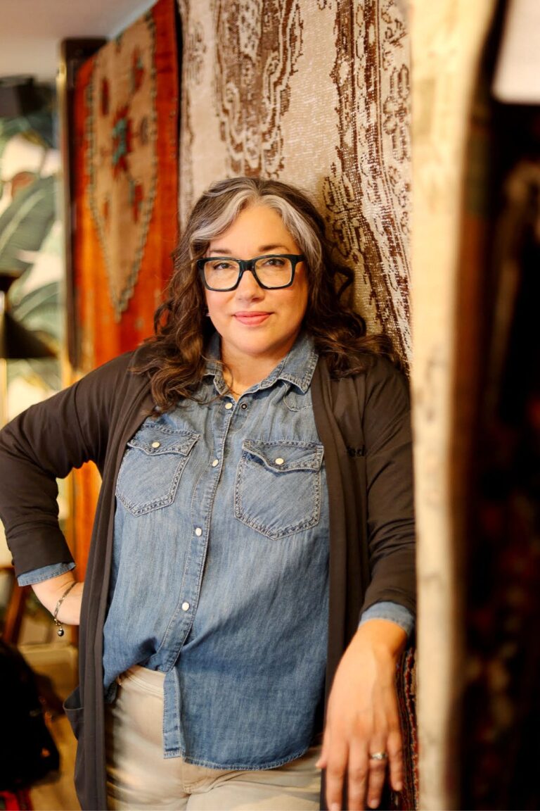 Woman wearing glasses standing in front of hanging rugs