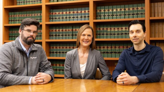 Three people sitting at table in front of book shelf