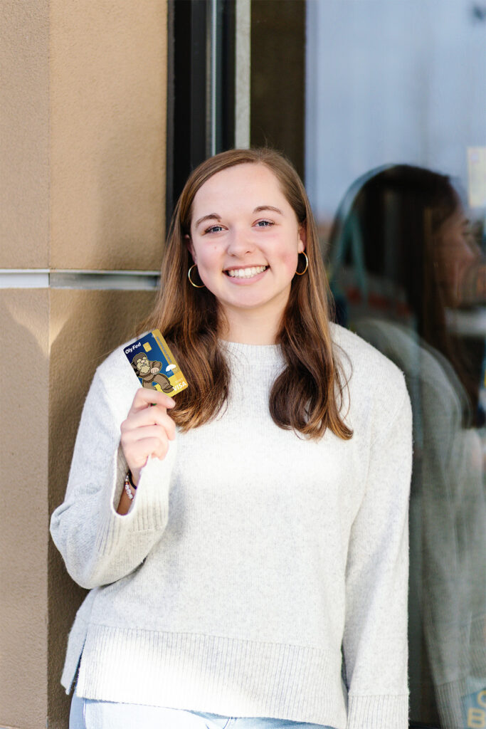 Olyfed employee with long brown hair in white sweater holding promotional centralia college card