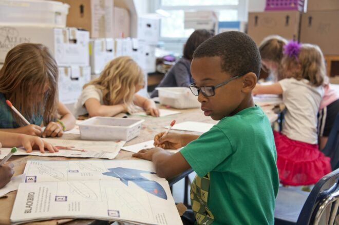 Group of children sitting at long table working in workbooks