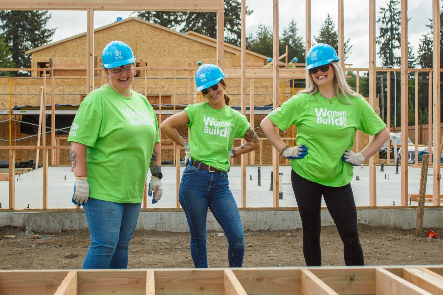Three women in hardhats stand on a residential home build site.