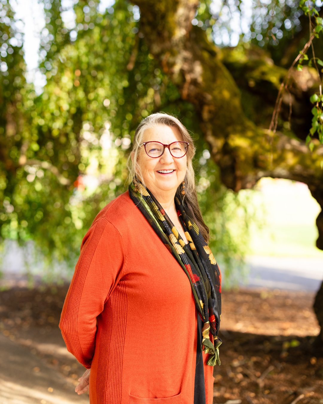 Gaylene VanWey, Employee, Administrative Assistant, Red/orange cardigan, standing under tree